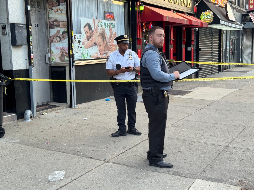 Two police officers standing on a sidewalk taped off with yellow crime scene tape in front of stores.