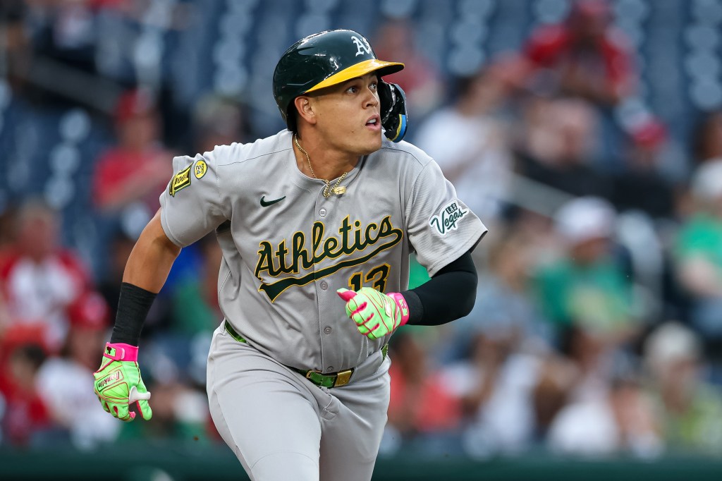 An Oakland Athletics player, wearing a green helmet and gray uniform with "Athletics" written in green, runs on a baseball field.