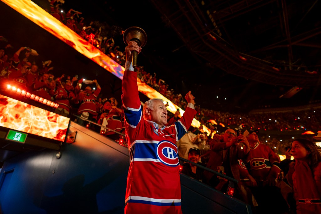 A Montreal Canadiens fan in a red jersey holding a torch in an arena with fire effects on screens.