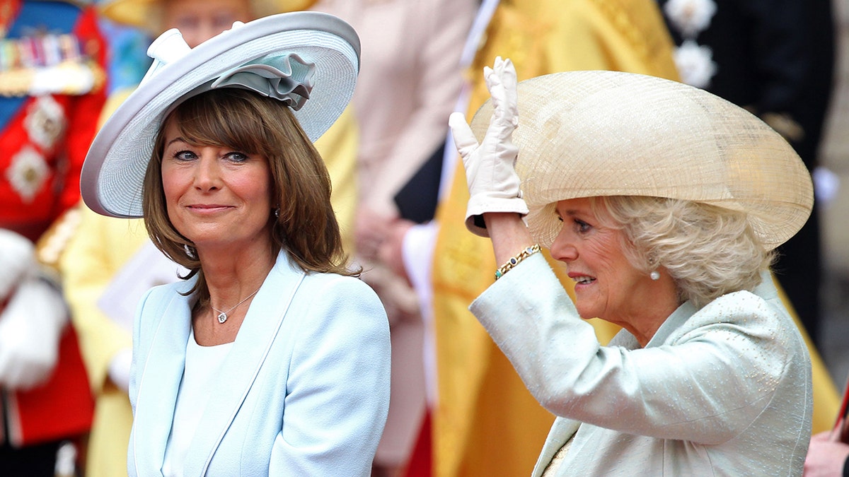 Carole Middleton smiling seated next to Queen Camilla waving to crowd