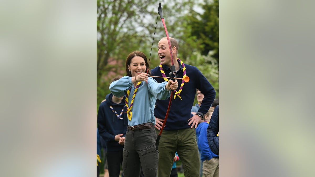 Catherine, Princess of Wales, shooting a bow and arrow while Prince William watches