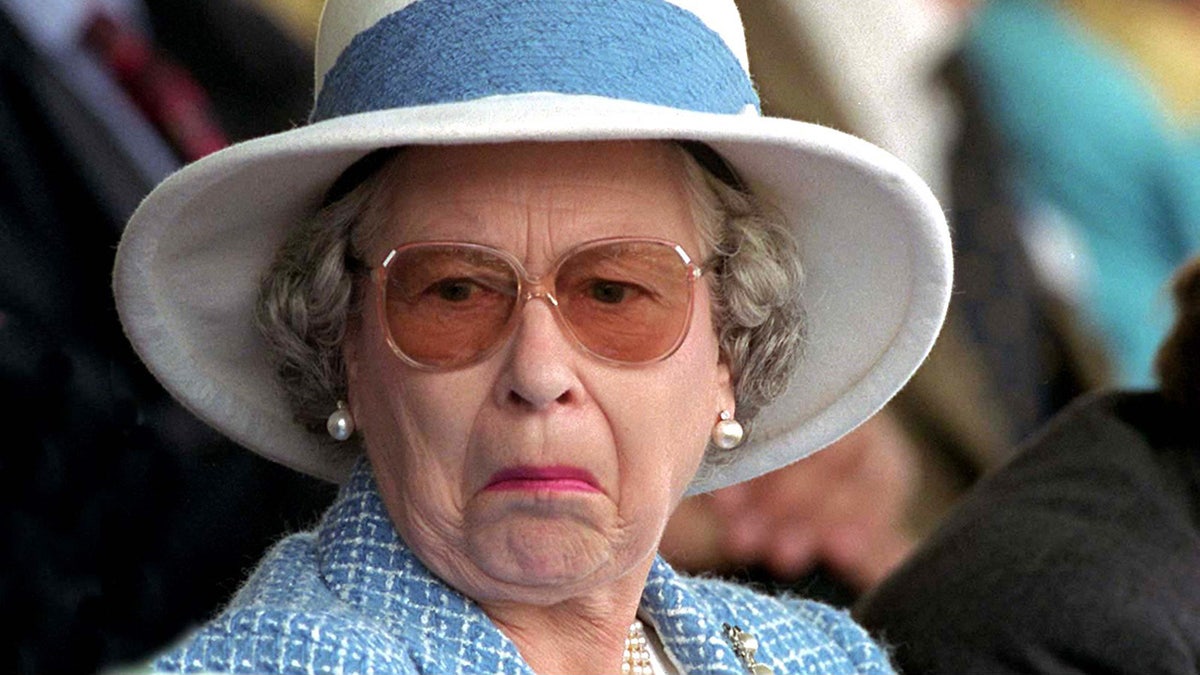 Queen Elizabeth II making a funny face wearing a blue and white suit and matching hat