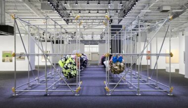 Art installation with geometric metal framework and colorful fabric spheres in a gallery setting with bright overhead lights.
