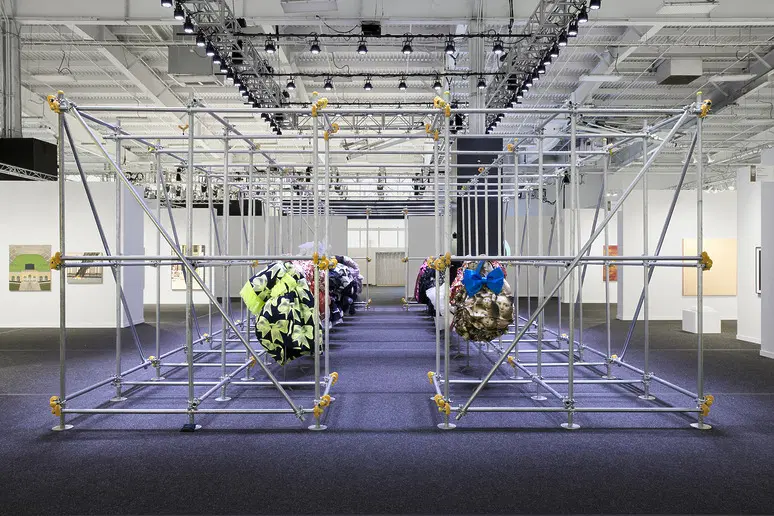 Art installation with geometric metal framework and colorful fabric spheres in a gallery setting with bright overhead lights.