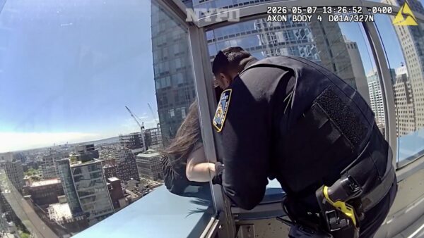 A police officer who identified himself as Nicholas holds the hand of a despondent woman on a 30th floor ledge over Downtown Brooklyn. Photo: NYPD video
