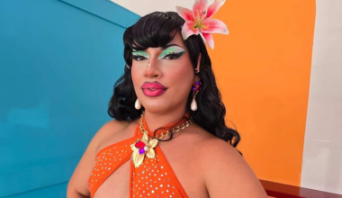Milwaukee drag queen Susie Starlet posing with a flower in her hair and an orange dress.