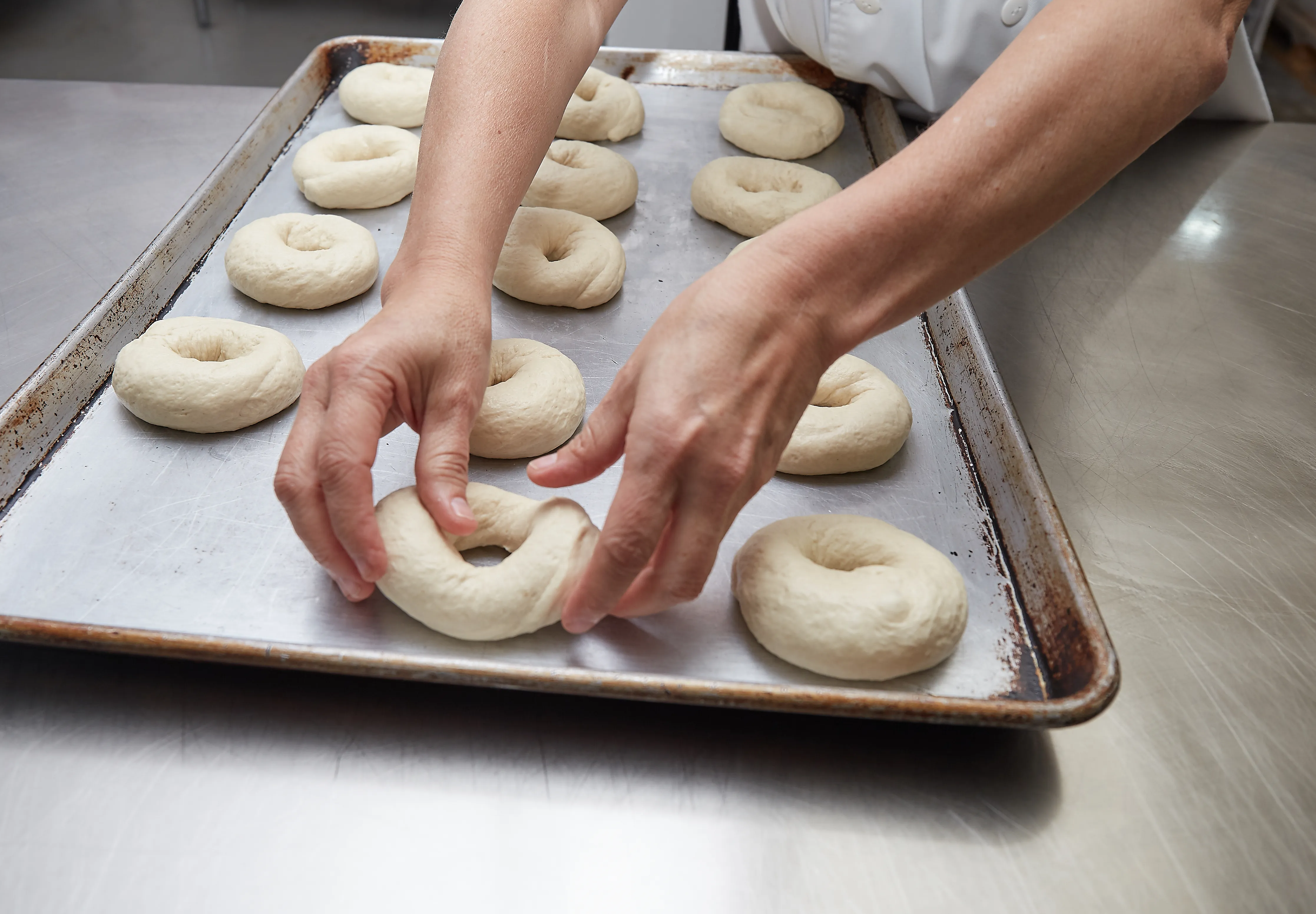 A baker preparing bagels on a metal baking sheet.