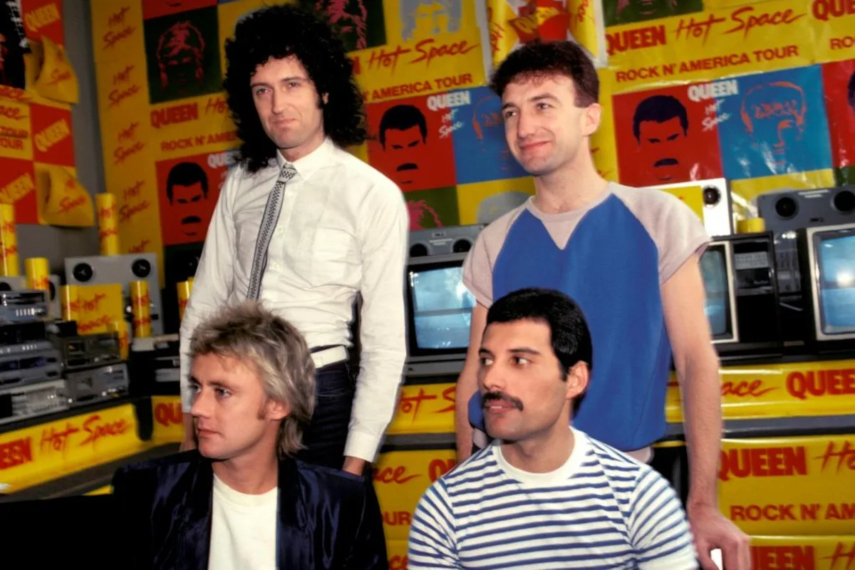Queen pose for a group portrait in front of posters for their Hot Space Rock N' America tour, 1982