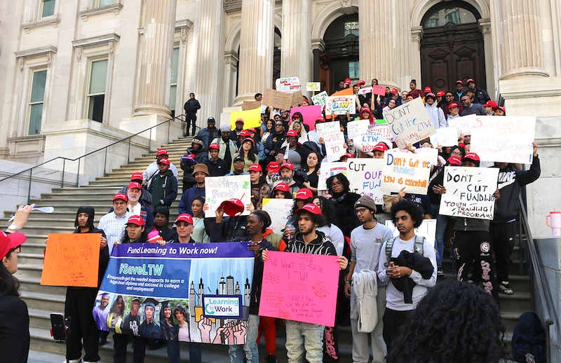 People hold signs outside a building with pillars.