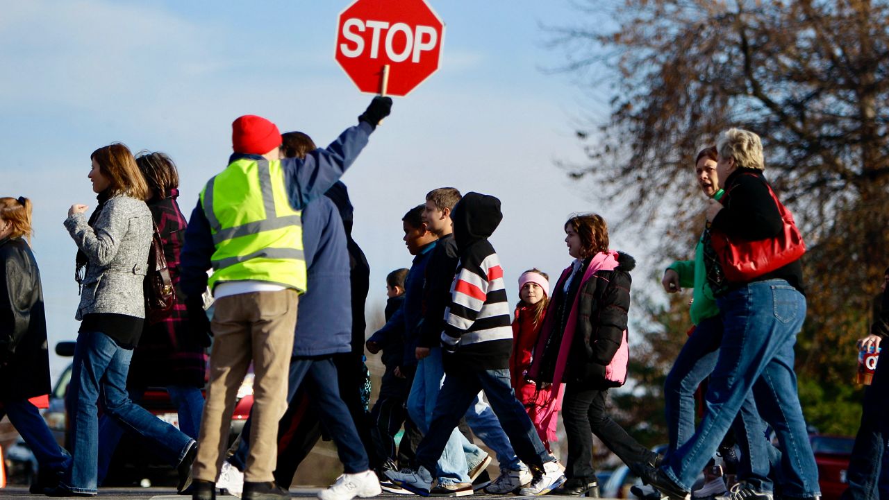 crossing guard holds up stop sign as students cross street
