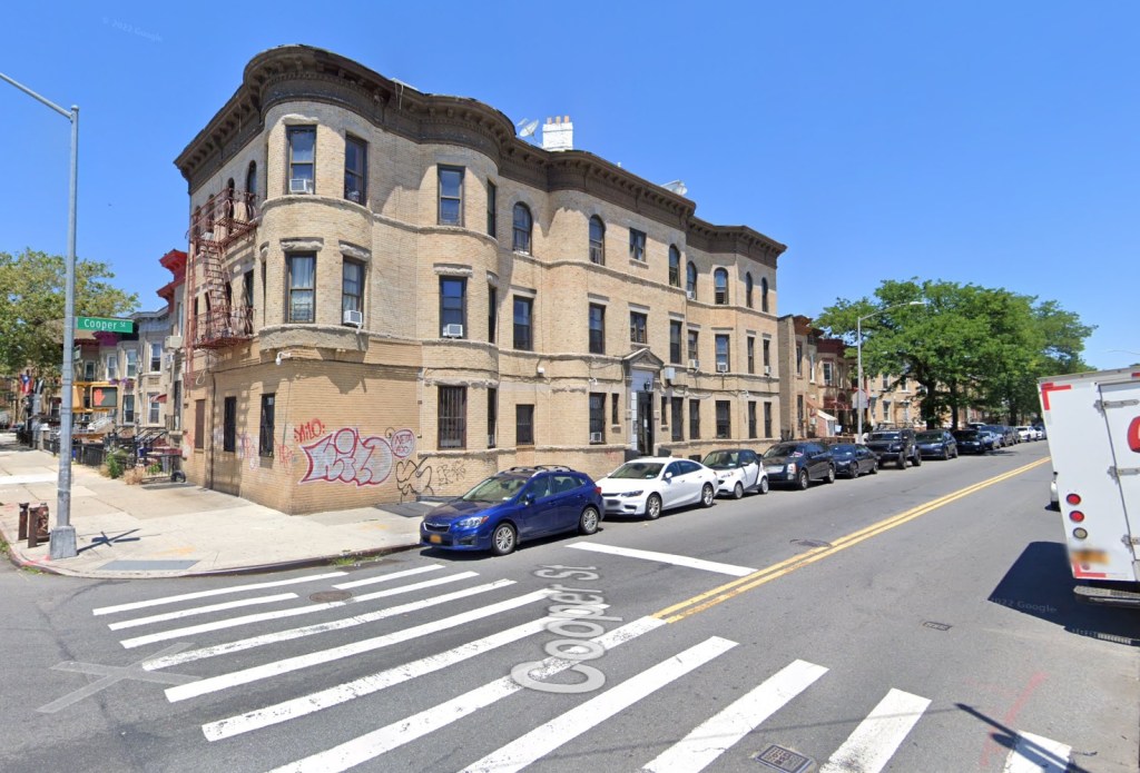 Street view of a beige brick building with curved bay windows at the corner of Cooper Street.
