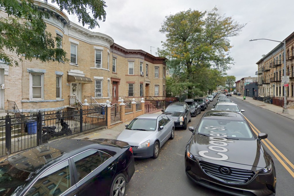 A street scene with cars parked on both sides of the road, and apartment buildings lining the left side.