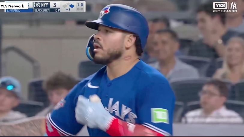 A baseball player from the Blue Jays stands with a bat in his hand, looking out at the pitcher during a game against the New York Yankees.