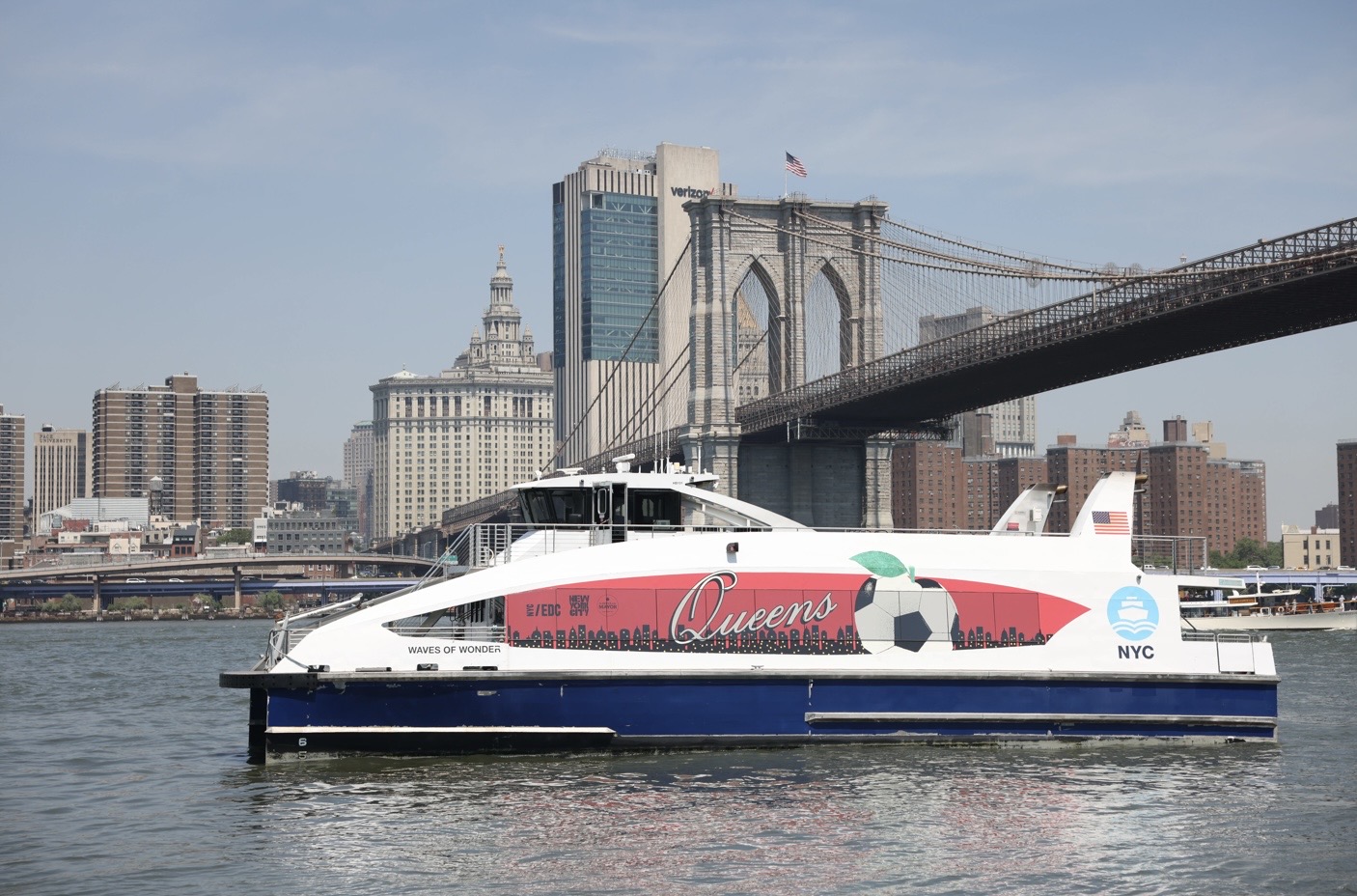 Five NYC Ferry vessels have been custom-wrapped to celebrate the identity of each borough. The Queens ferry, “Waves of Wonder,” is shown next to the Brooklyn Bridge. Photo: NYCEDC