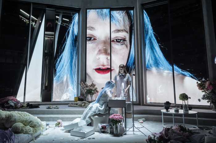 two women on a stage with one looking in a mirror