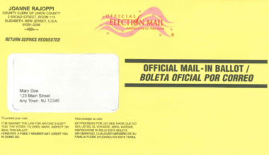 A photo of a yellow vote-by-mail ballot envelope.