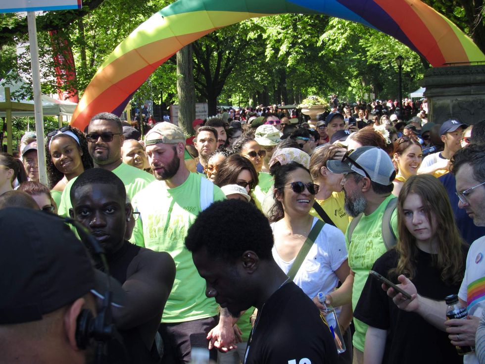 A crowd of people gather beneath a rainbow archway.