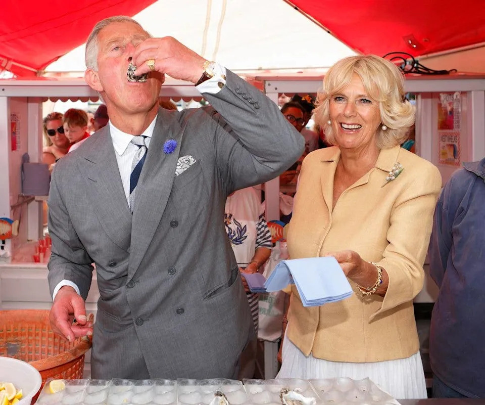 King Charles swallowing an oyster with Queen Camilla