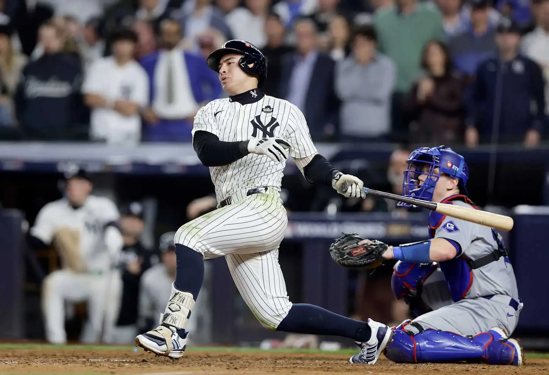 Yankees player swings bat during a game with fans in the background.