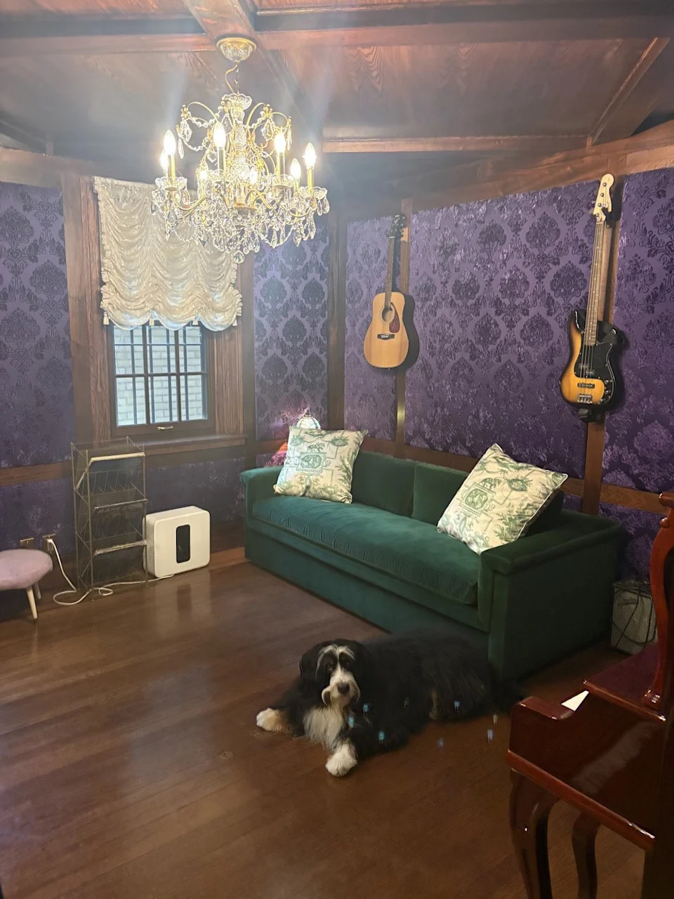 The room's jewel-toned color scheme includes purple Damask wall panels, red mahogany wood, and an emerald green sofa.