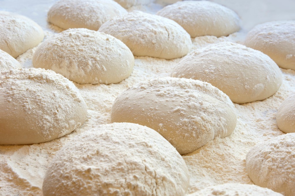 Risen pizza or bread dough balls, floured and ready for baking.