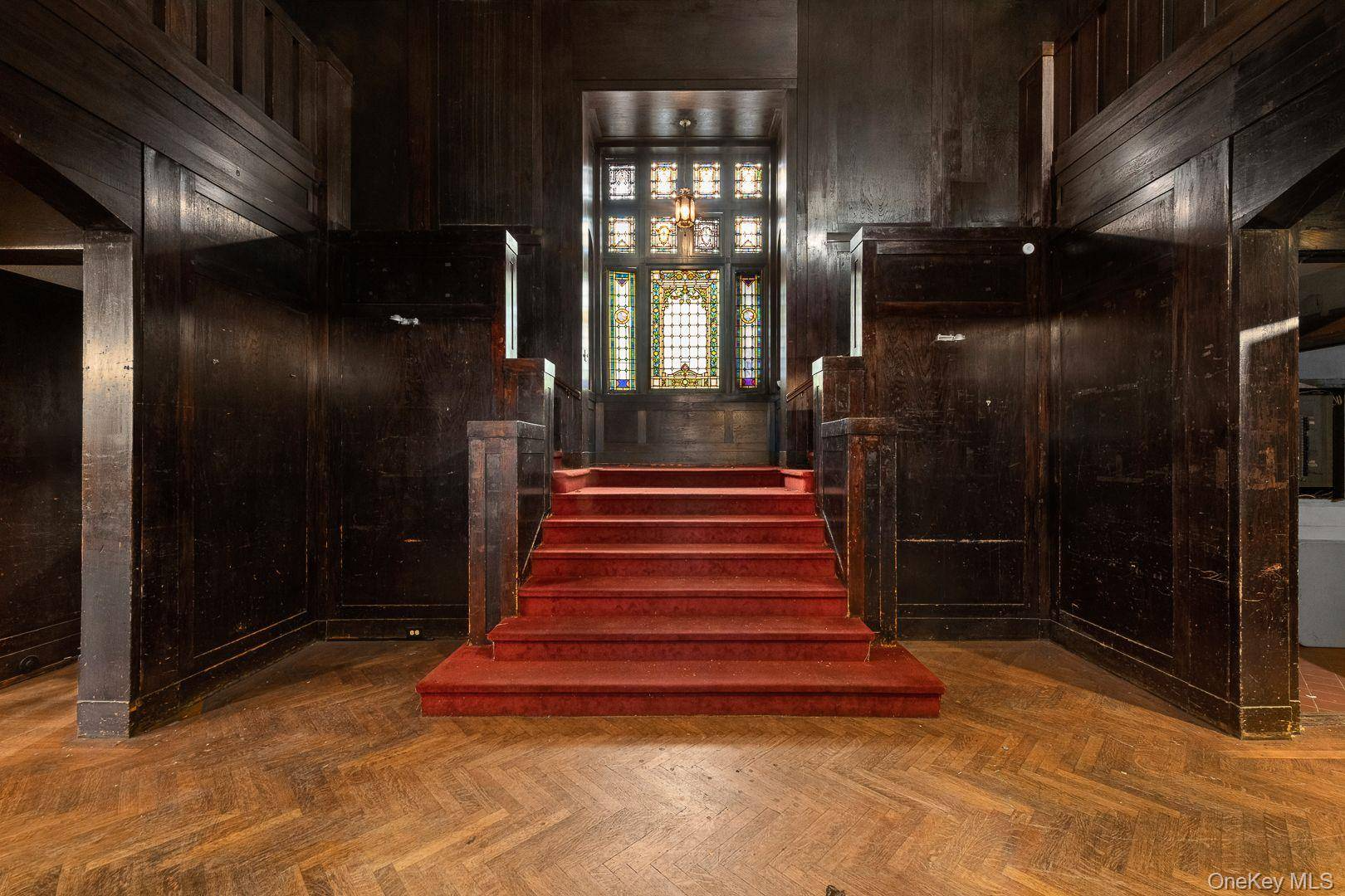 entry hall with red carpeted stairs, stained glass window on landing