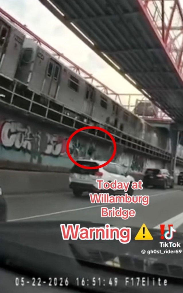 Video still of two people on top of a moving J train under the Williamsburg Bridge.