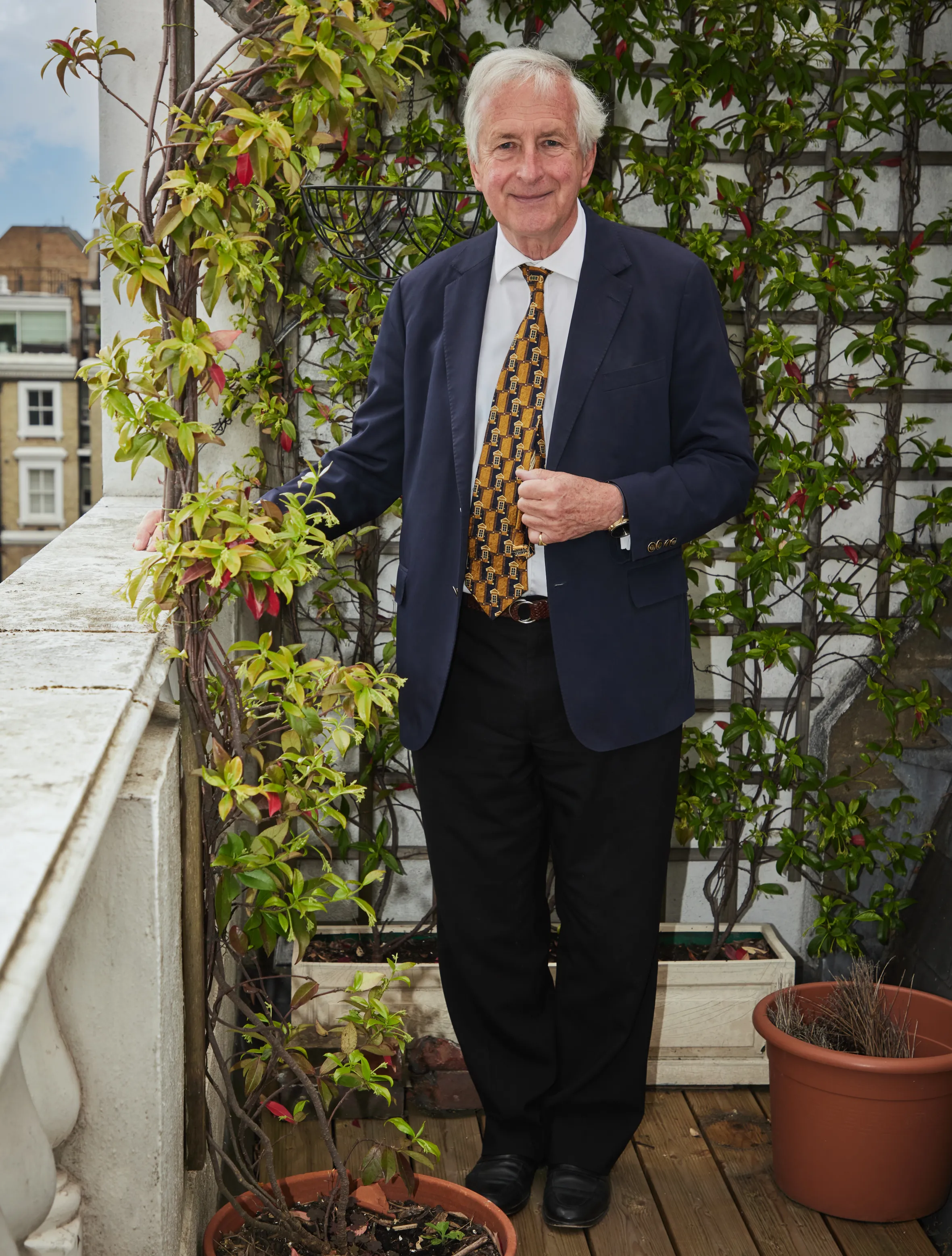 Hugo Vickers at home in London, standing on a balcony with plants.