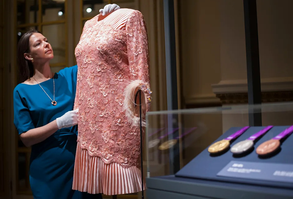 Curator Caroline de Guitaut adjusts a peach cocktail dress designed by Angela Kelly and worn by Queen Elizabeth II's at the opening Ceremony of the London 2012 Olympic games, during a press preview for Fashioning a Reign: 90 Years of Style from The Queen's Wardrobe, an exhibition at Buckingham Palace in London.