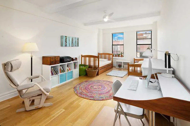Bright room with two wooden beds, a desk with a computer, a colorful rug, and a cozy reading chair.