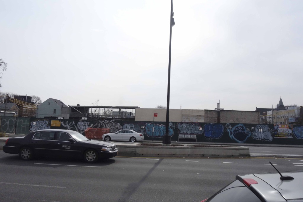 road with site behind surrounded in green construction fence