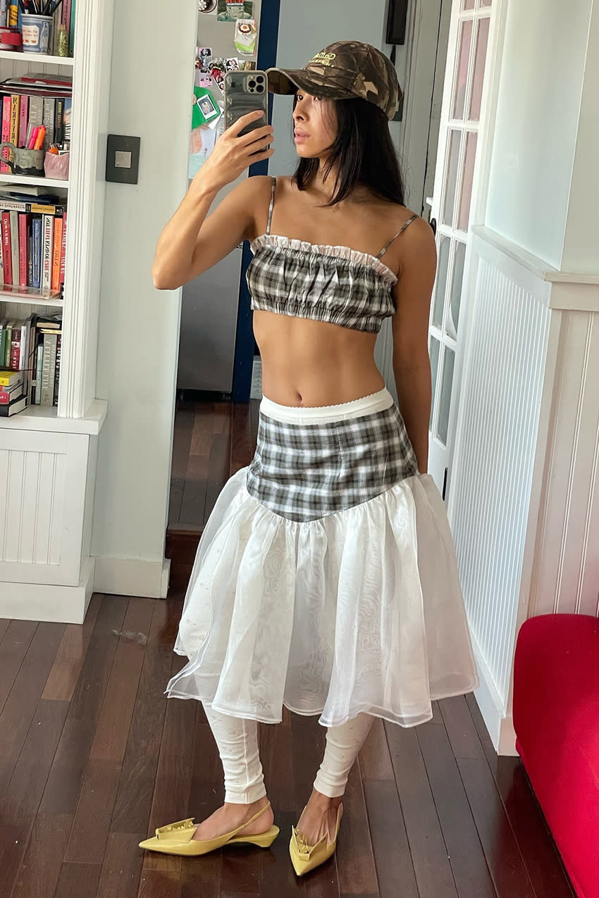 a woman wearing a plaid cropped tank top, a plaid and white drop waist skirt, and yellow sling back kitten heels. 