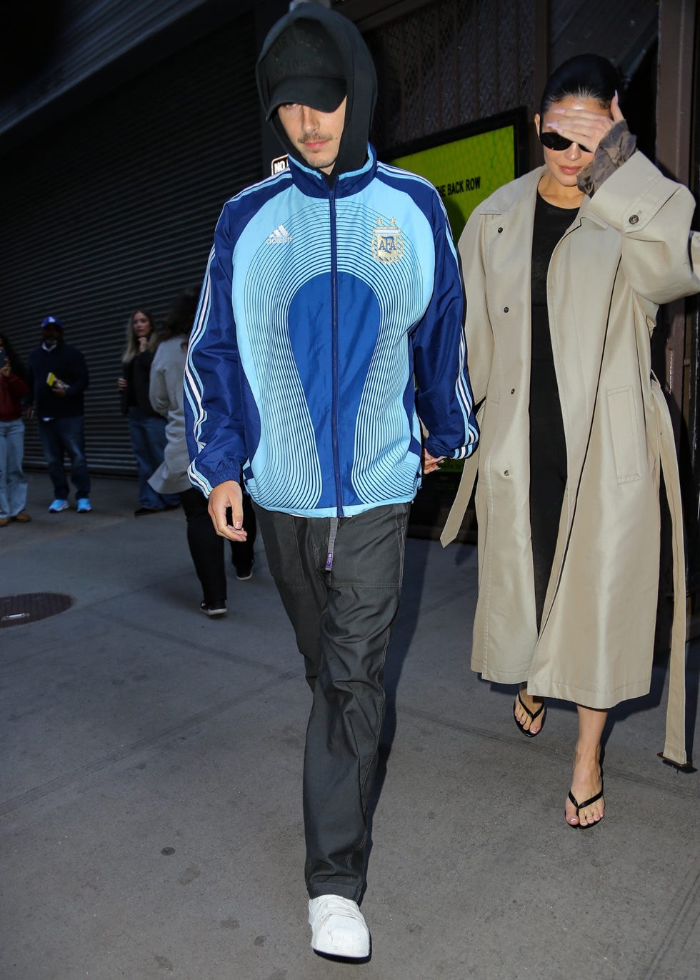 Two individuals walking on a city street, one wearing a sports jacket and the other in a trench coat. Two individuals walking on a city street, one wearing a sports jacket and the other in a trench coat.
