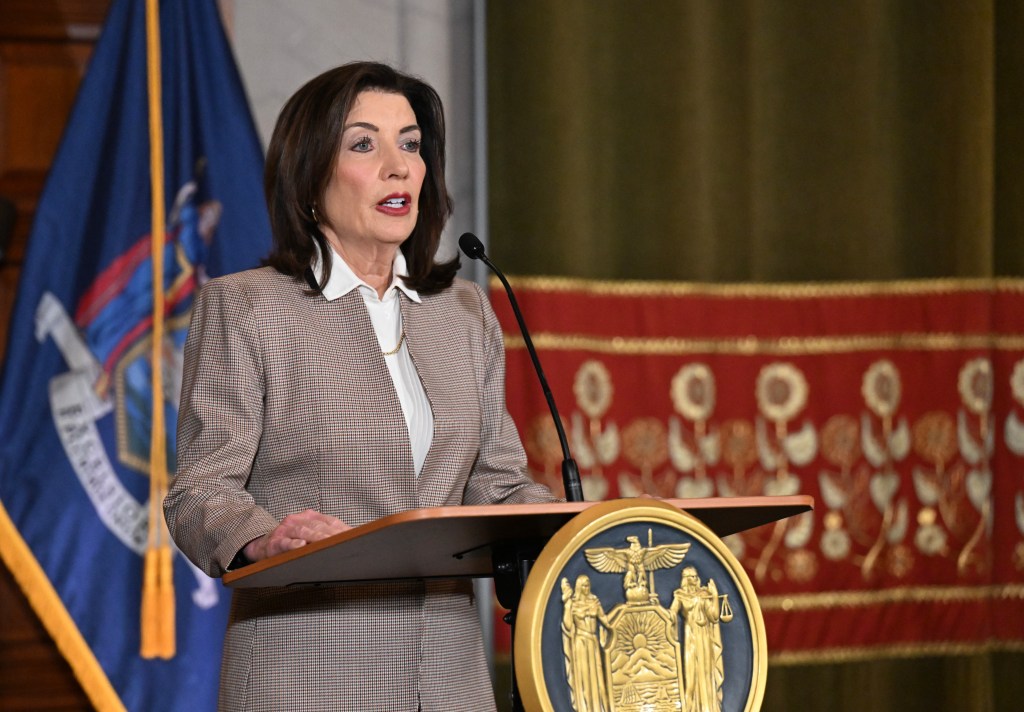 Gov. Kathy Hochul speaks at a podium with a New York state seal, with a blue flag behind her.