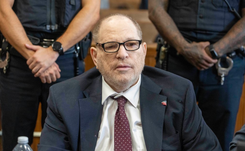 Harvey Weinstein at his trial with two police officers standing behind him.