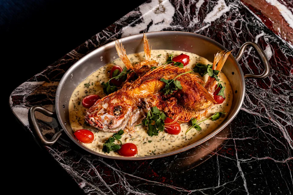 Whole roasted snapper with herbs and cherry tomatoes served in a pan at ilili Midtown NYC