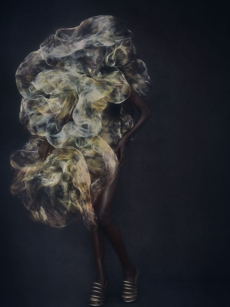 Model wearing voluminous metallic organza dress with swirling translucent layers and sculptural silhouette.
