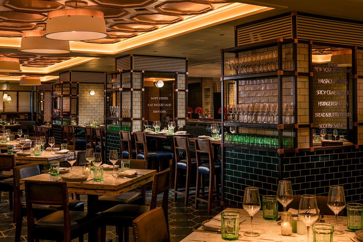 The dining room of Legasea Bar and Grill at Moxy Times Square, featuring subway tiles, leather chairs, and mirrors listing menu items like the signature spicy crab beignet.