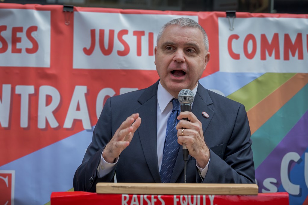 Mario Cilento, NYS AFL-CIO President, speaking at a rally with a banner in the background.