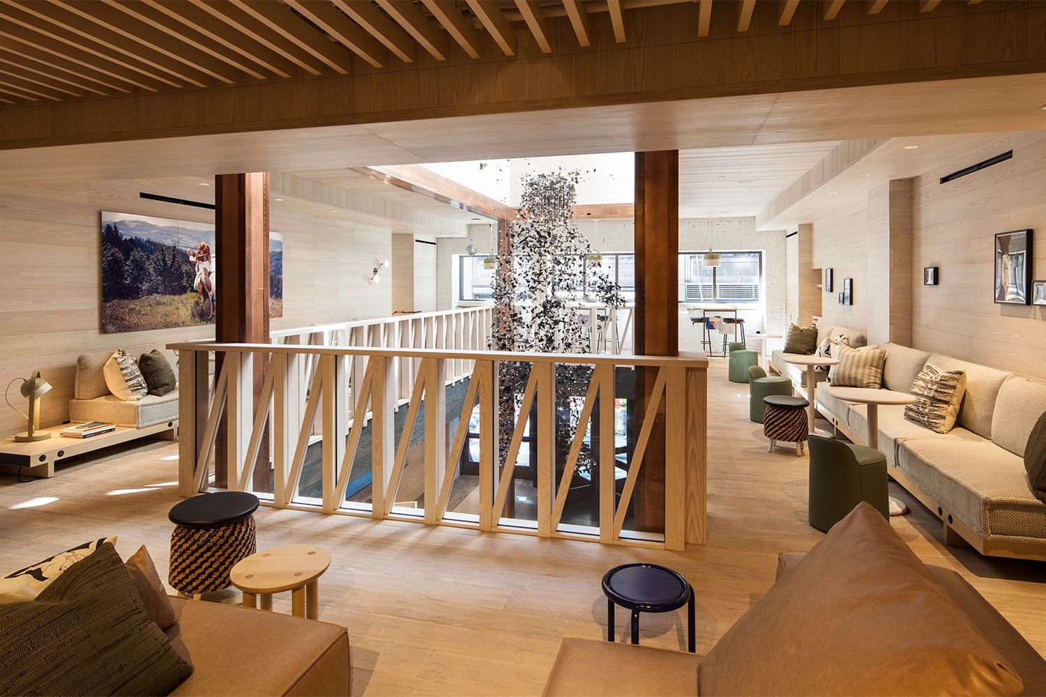 Bright, wood-paneled second-floor lobby lounge at Moxy Times Square featuring flexible seating and a view of the hanging bear installation in the atrium.