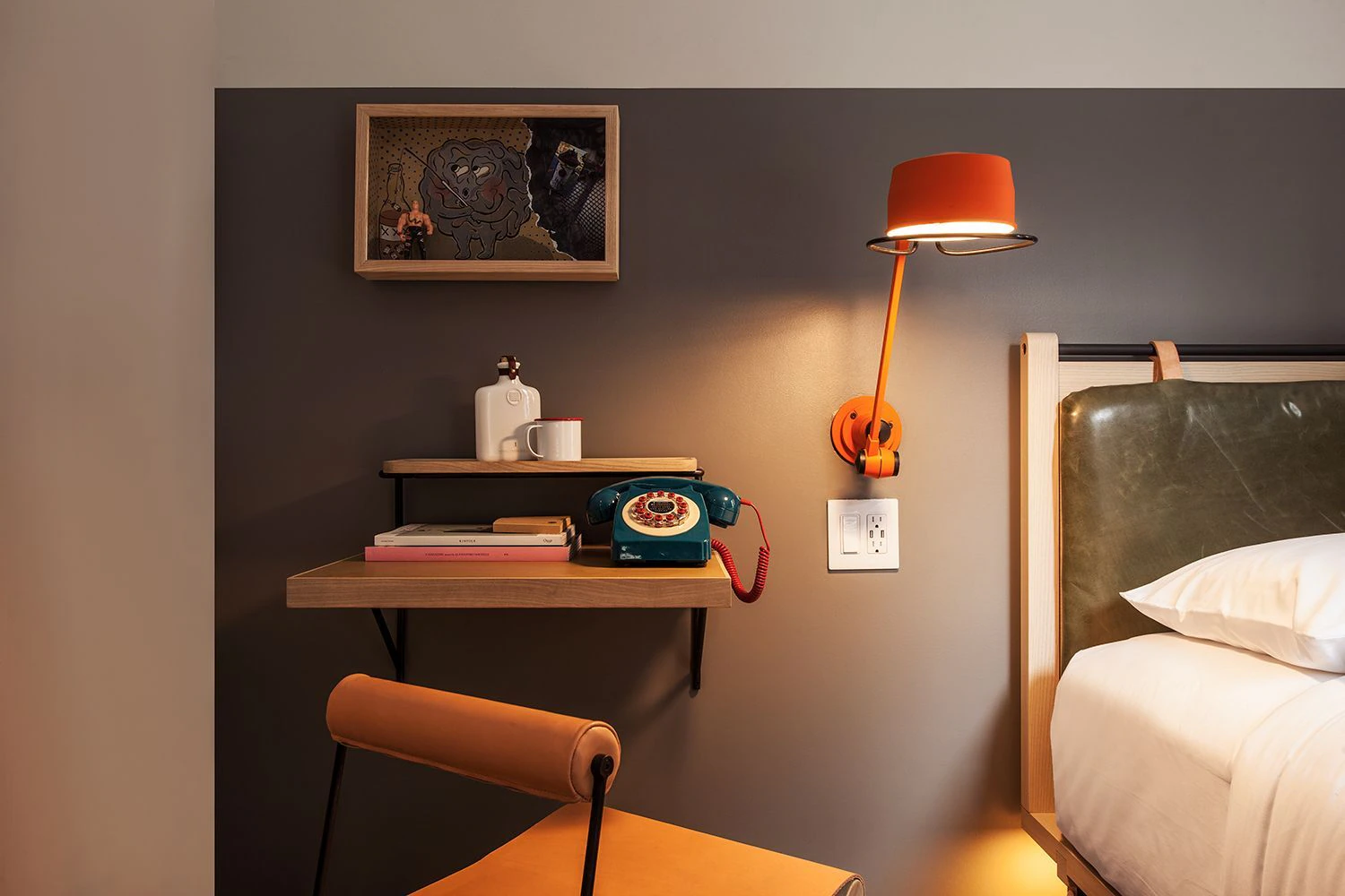 Close-up of the foldaway desk in a Moxy Times Square guestroom, featuring a teal retro phone, orange reading lamp, and a foldable leather chair.