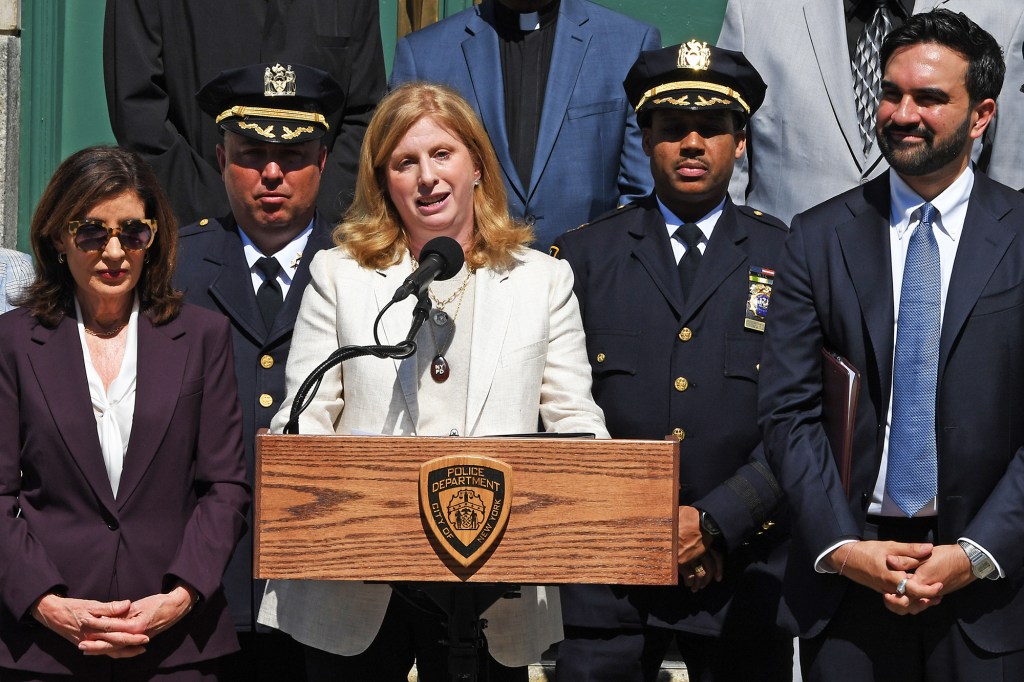 New York Police Commissioner Jessica Tisch speaking at a podium, flanked by Governor Kathy Hochul, two police chiefs, and Mayor Zohran Mamdani.