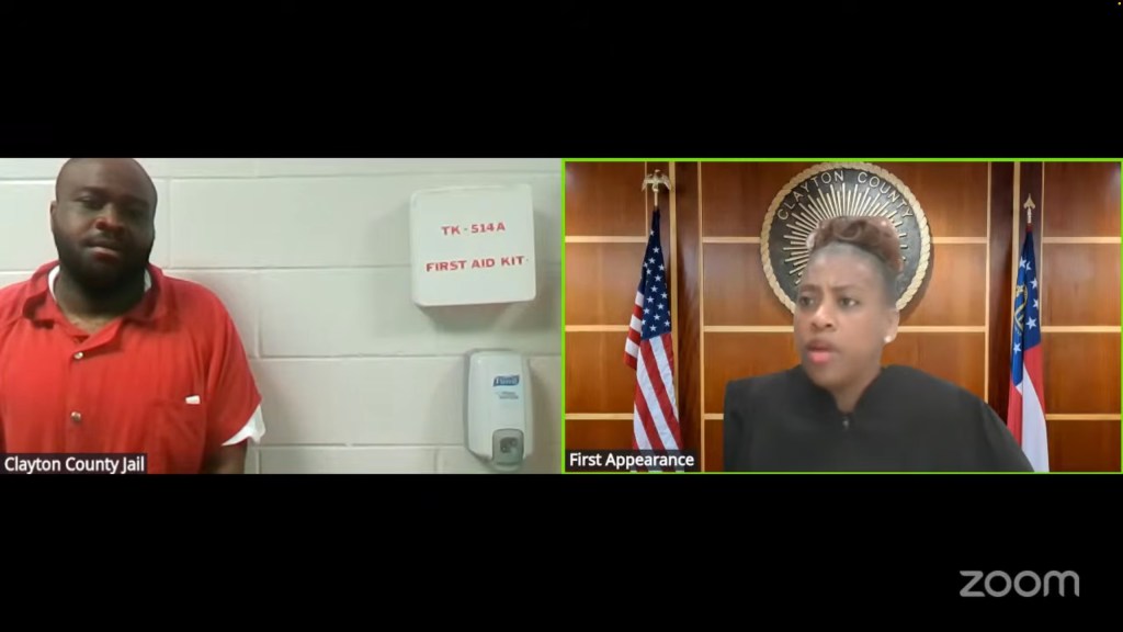 A split screen image showing Oreoluwa Oloruntoba in an orange jumpsuit on the left, labeled "Clayton County Jail," and a female judge in a black robe on the right, labeled "First Appearance."