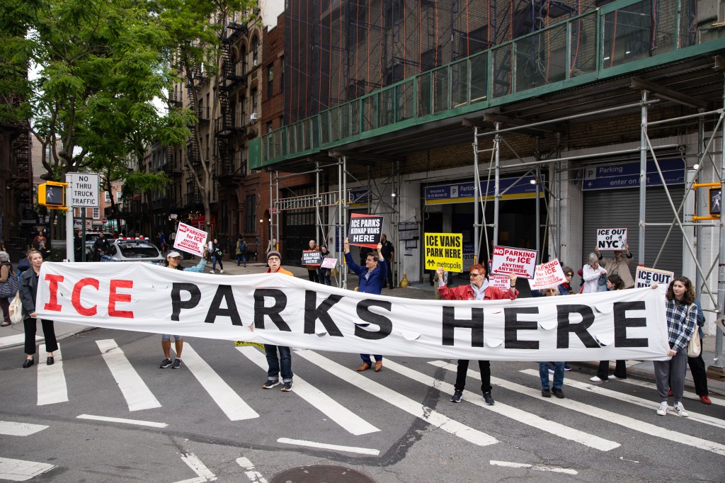 A protest in New York City with people holding a large banner that reads "ICE PARKS HERE" and signs against ICE parking in a Metropolis Garage.
