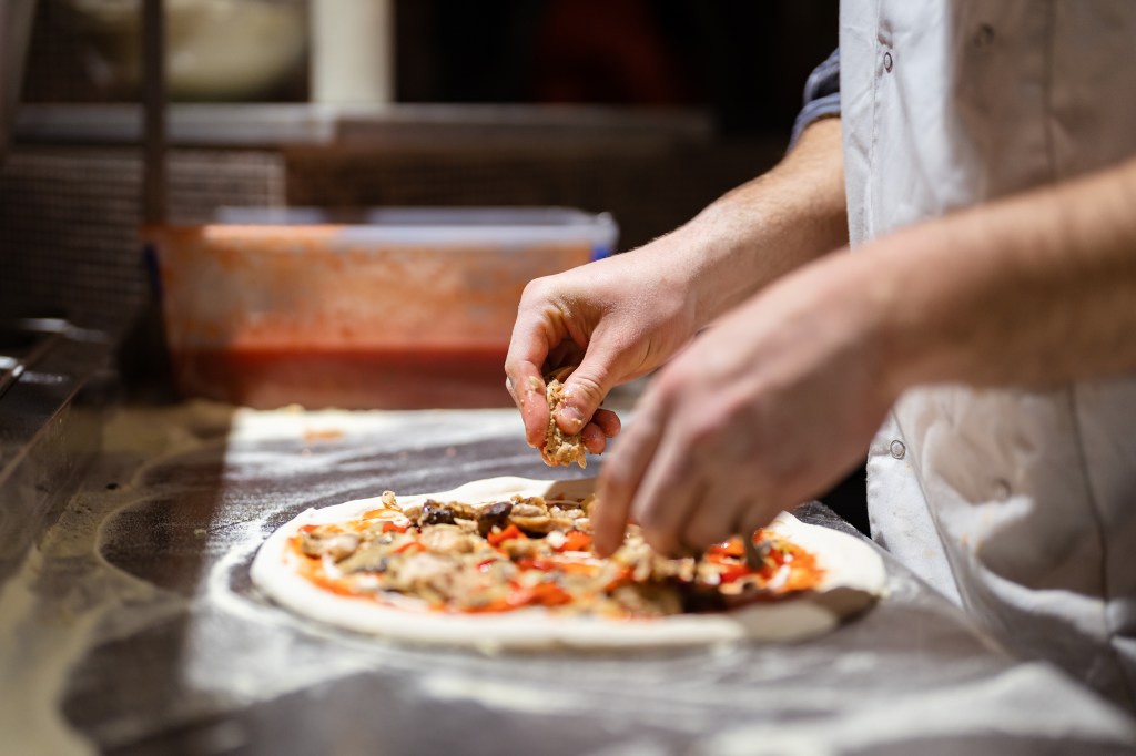 Chef's hands preparing a pizza with toppings.