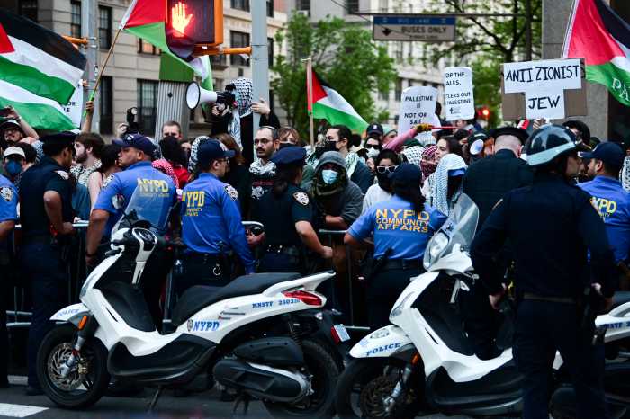 police officers and protestors at a demonstration with some protestors in masks and holding Palestinian flags