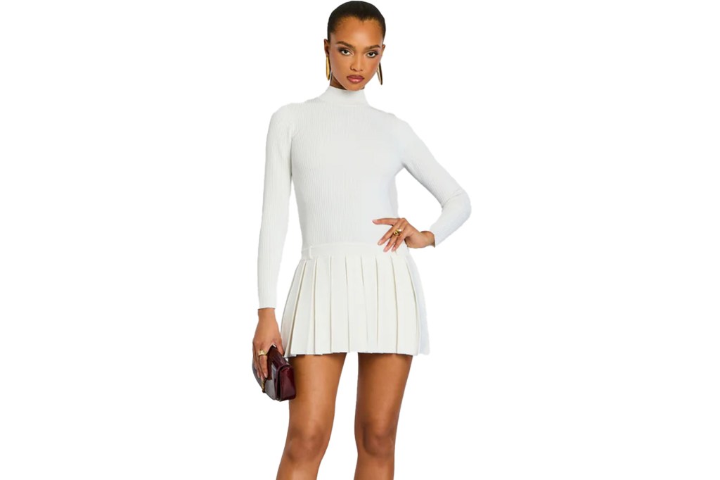 Woman in a white turtleneck and pleated skirt holding a burgundy clutch.