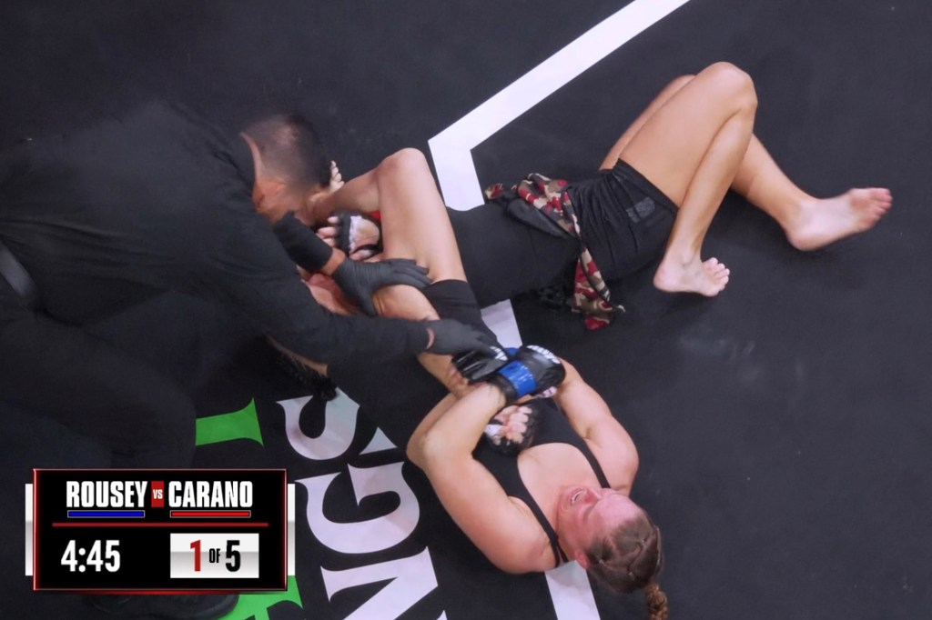 MMA fighter Ronda Rousey on the ground with a referee attempting to intervene in a match against Carano.
