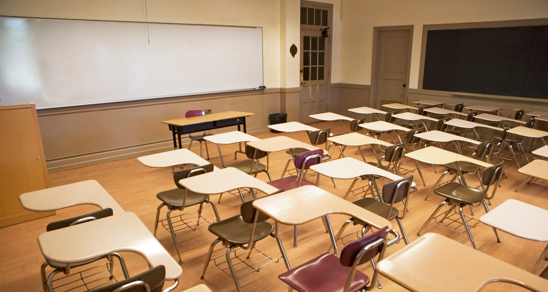 Empty classroom with rows of desks and chairs, a whiteboard at the front, and a wooden floor.