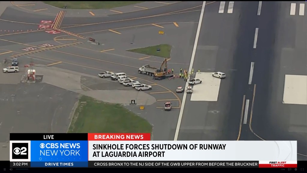 An aerial view of a sinkhole on a LaGuardia Airport runway with construction vehicles and workers.